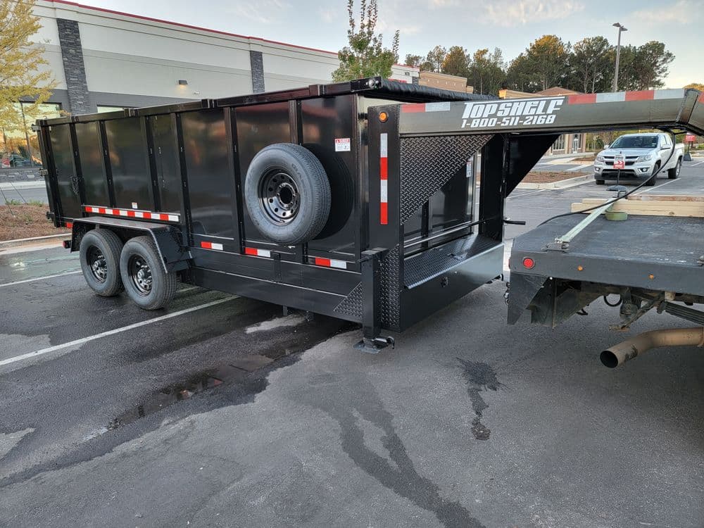 Black utility trailer with a spare tire, parked on asphalt near a business area.