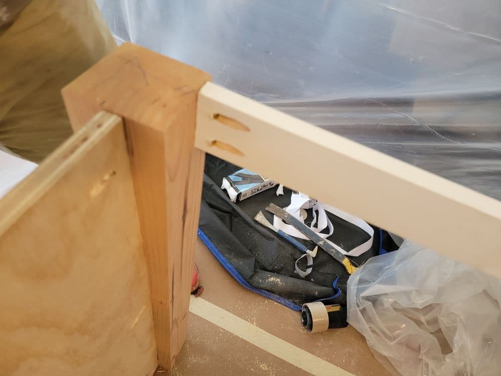 Close-up of a wooden joint in a carpentry project, with tools and materials in the background.