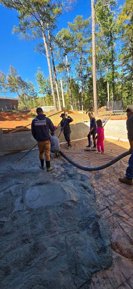 Workers pouring concrete in a forested area, with children observing the construction process.