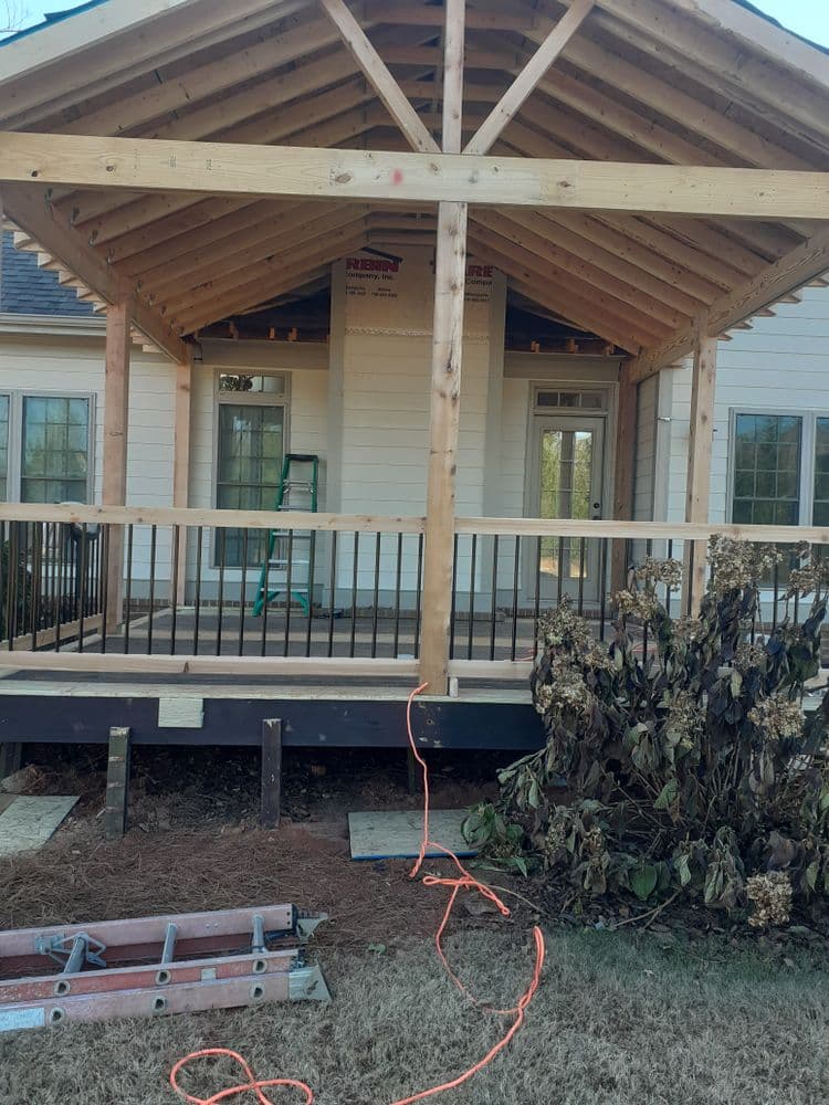 Under-construction porch with wooden beams, railing, and tools in a residential setting.