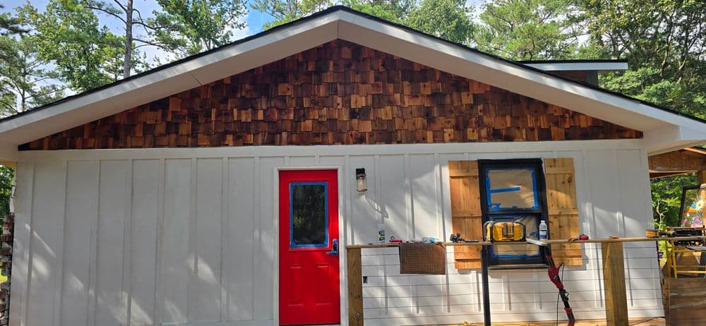 Modern cabin exterior with red door, wooden shingles, and natural surroundings.