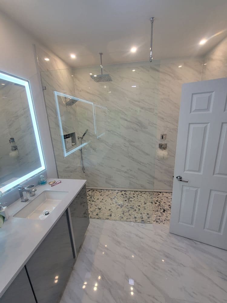 Modern bathroom with marble walls, walk-in shower, and sleek vanity with mirror lighting.