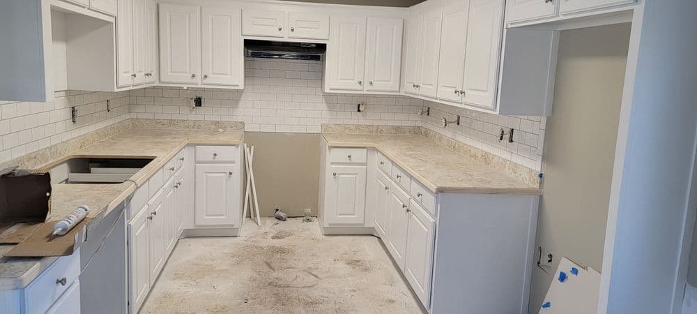 Modern kitchen renovation with white cabinets, marble countertops, and subway tile backsplash.