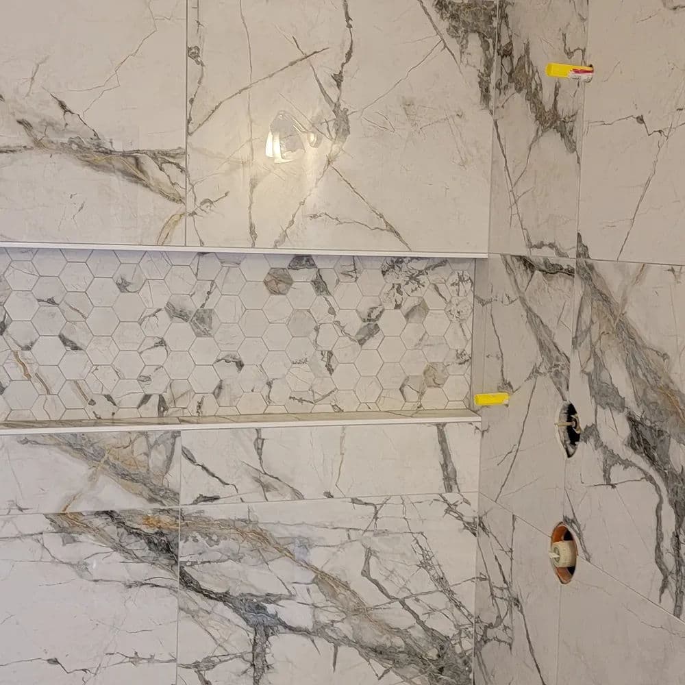 Modern bathroom shower walls featuring marble tiles and a hexagon mosaic niche.