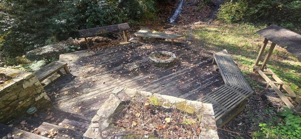 Wooden fire pit area surrounded by benches and foliage in a tranquil outdoor setting.