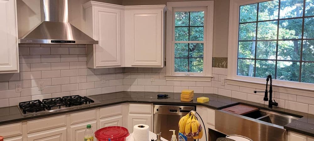 Modern kitchen with white cabinets, stainless steel appliances, and large windows overlooking greenery.