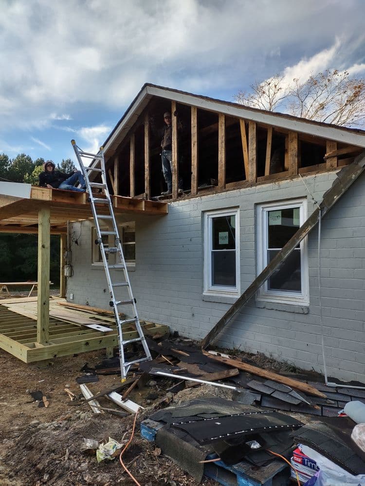 Home renovation project with two workers on the roof and a ladder outside a partially demolished house.
