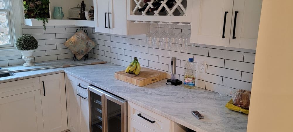 Modern kitchen with white cabinetry, marble countertop, wine fridge, and hanging glasses.