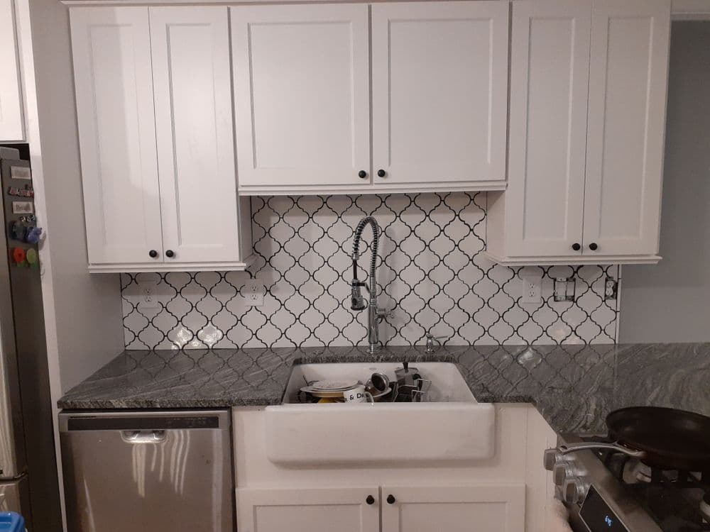 Modern kitchen with farmhouse sink, granite countertops, and tiled backsplash, featuring dishes.