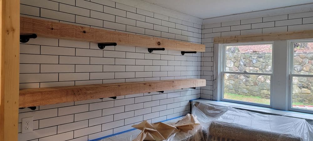 Rustic wood shelves against a white tiled wall in a cozy, under-construction room.