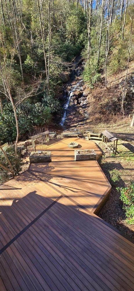 Wooden deck with seating area overlooking a serene water feature in a wooded landscape.