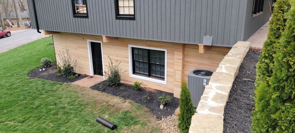 Modern home exterior with wood siding, landscaping, and stone wall features.