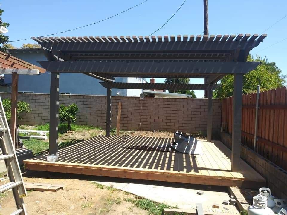 Wooden pergola structure in backyard with foundation and wooden deck in progress.