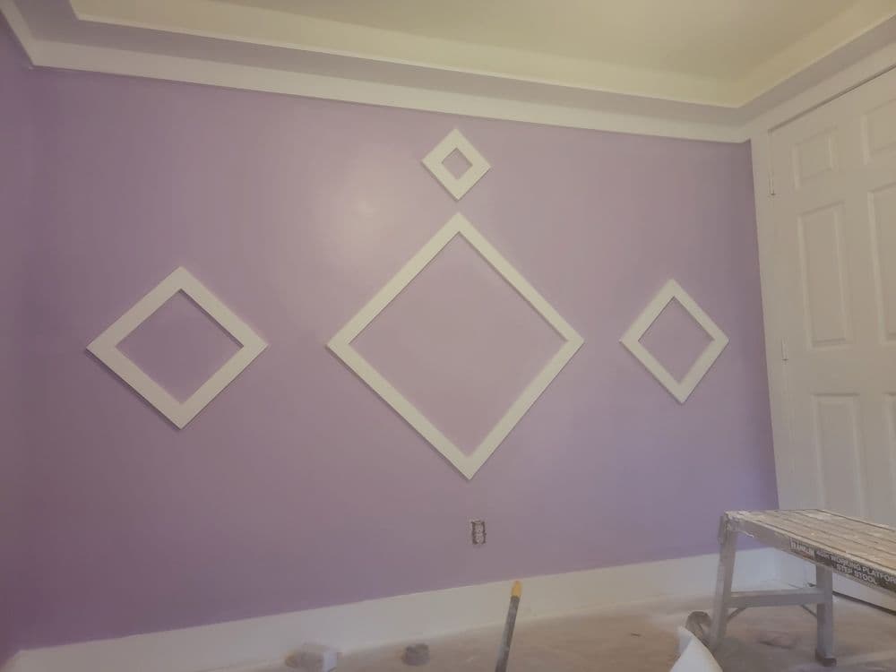 Purple accent wall with white diamond-shaped frames arranged artistically, paint tools nearby.