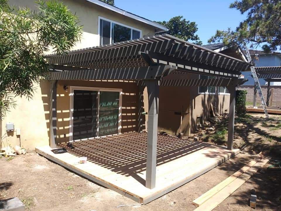 Newly built wooden pergola and deck in a backyard, featuring striped sunlight patterns.