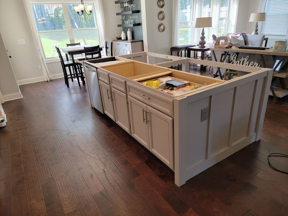 Modern kitchen with a partially assembled island and wooden flooring, featuring a dining area.