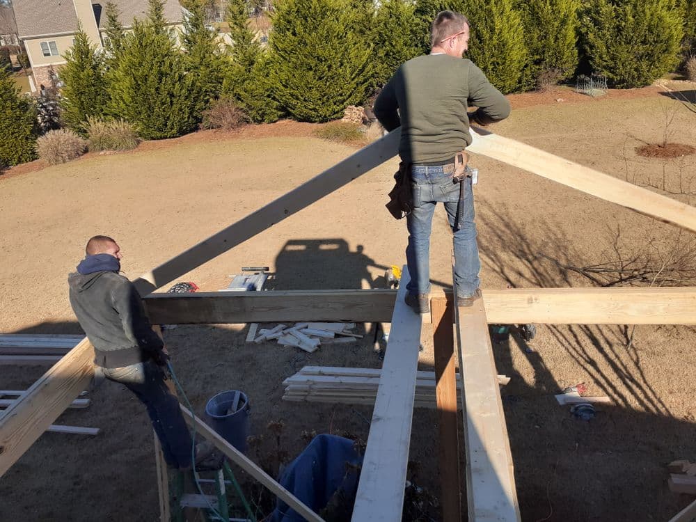 Two builders constructing a wooden structure on a sunny day in a residential yard.