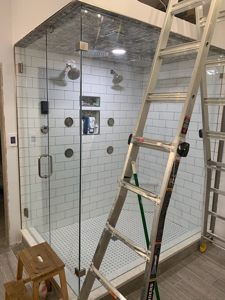 Modern glass shower installation with dual rain showerheads and ladder in a renovated bathroom.