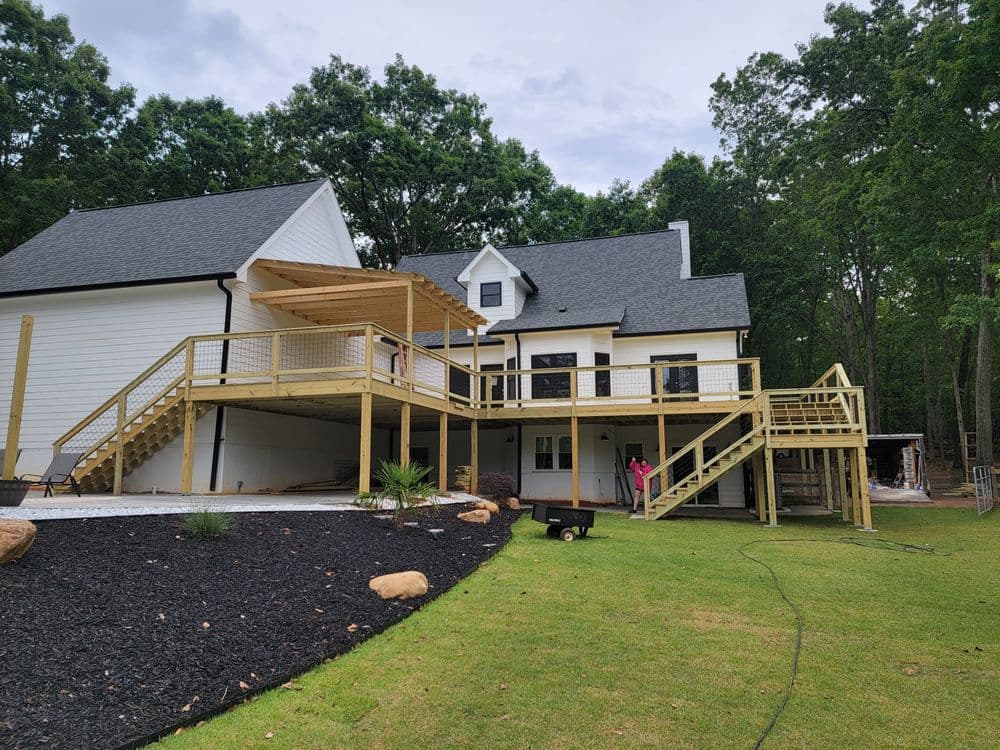 Newly constructed wooden deck attached to a modern house, surrounded by greenery and landscaping.