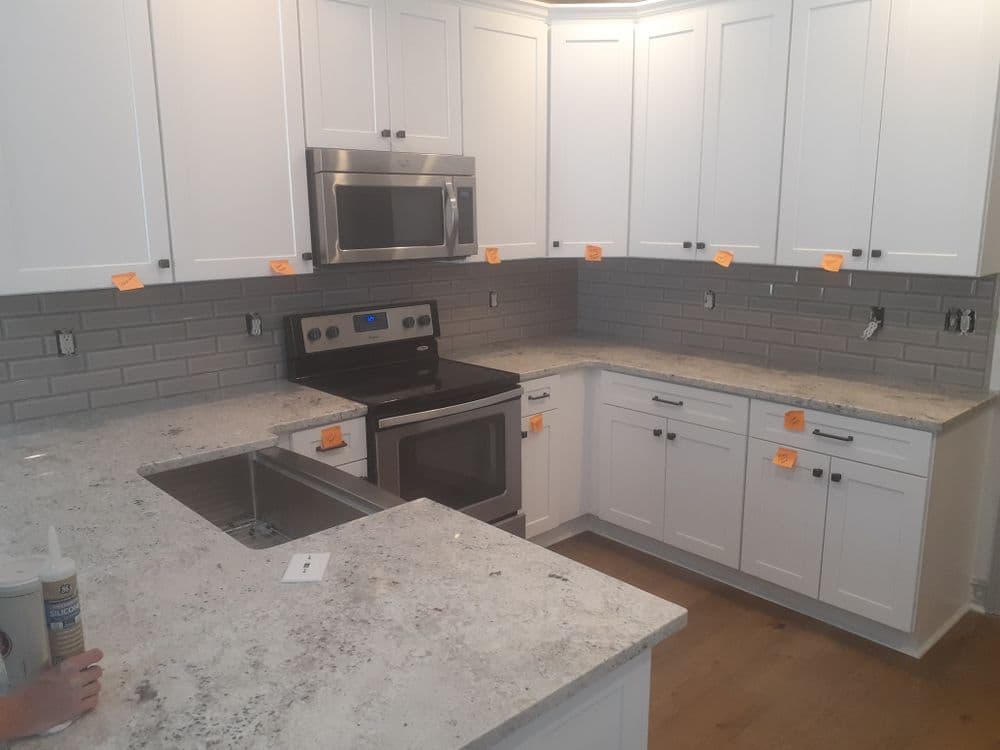 Modern white kitchen with granite countertops, stainless steel appliances, and gray backsplash tiles.