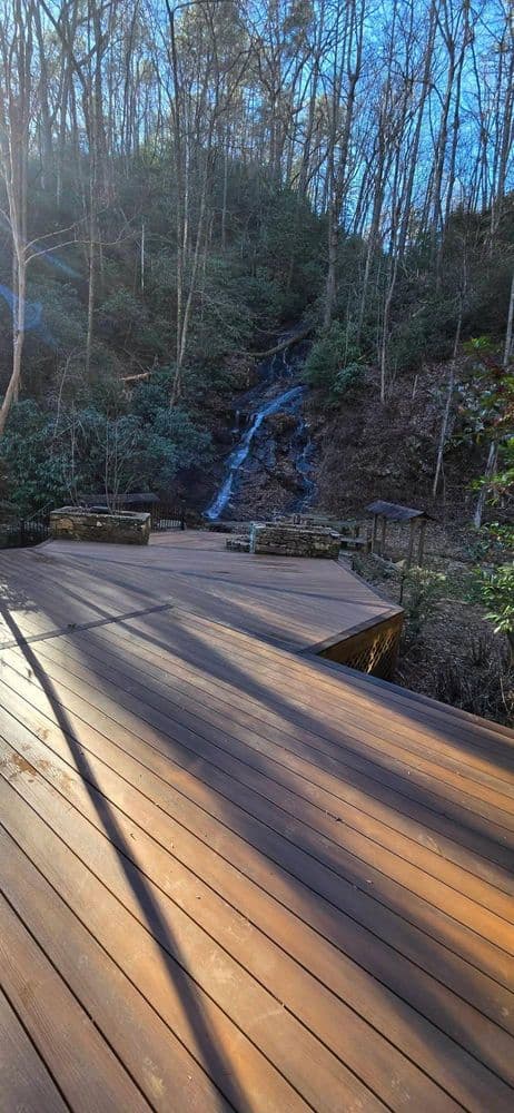 Wooden deck leads to a serene waterfall in a wooded area with lush greenery.
