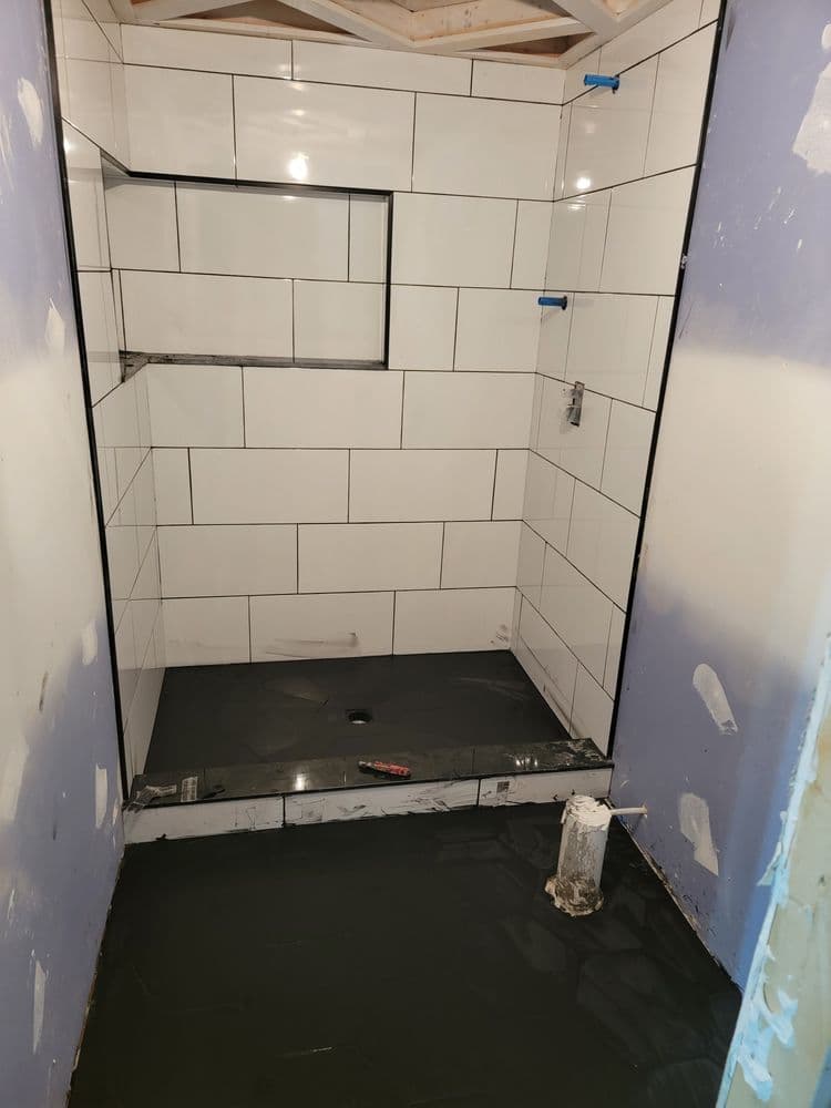Renovated bathroom with white tiled walls and a wet concrete floor before finishing touches.