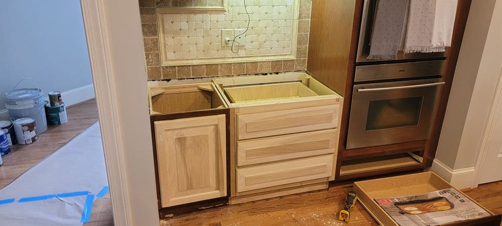 Kitchen renovation progress: empty cabinet frames with backsplash and appliances in view.