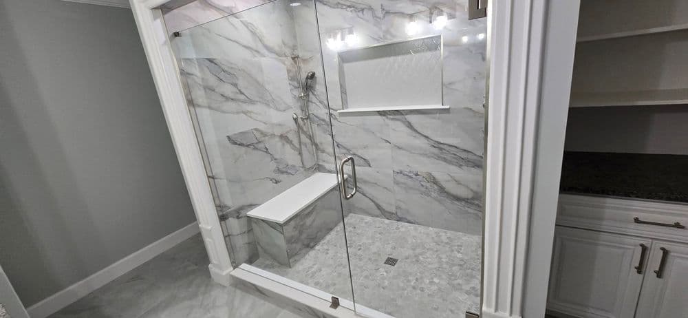 Modern walk-in shower with marble walls and bench, featuring glass enclosure and sleek design.