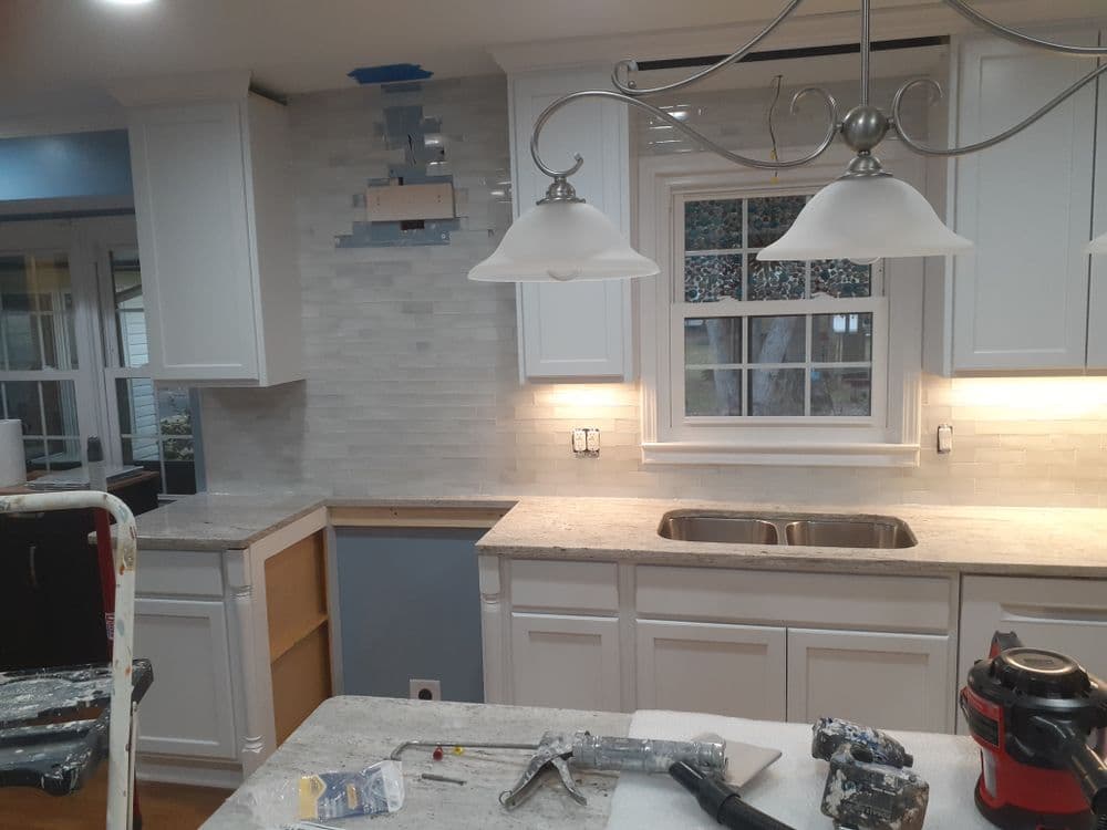 Modern kitchen renovation featuring white cabinetry, marble backsplash, and pendant lighting.