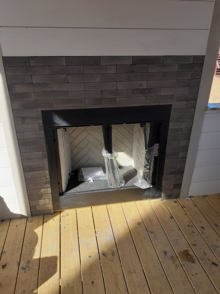 Modern fireplace with gray tile surround and herringbone pattern, partially installed in a wooden room.