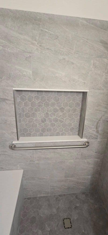 Modern bathroom with hexagon tile niche, stainless steel grab bar, and sleek gray stone walls.