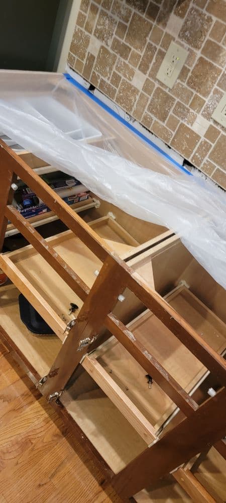 Kitchen cabinet renovation in progress with plastic covering and open drawers.