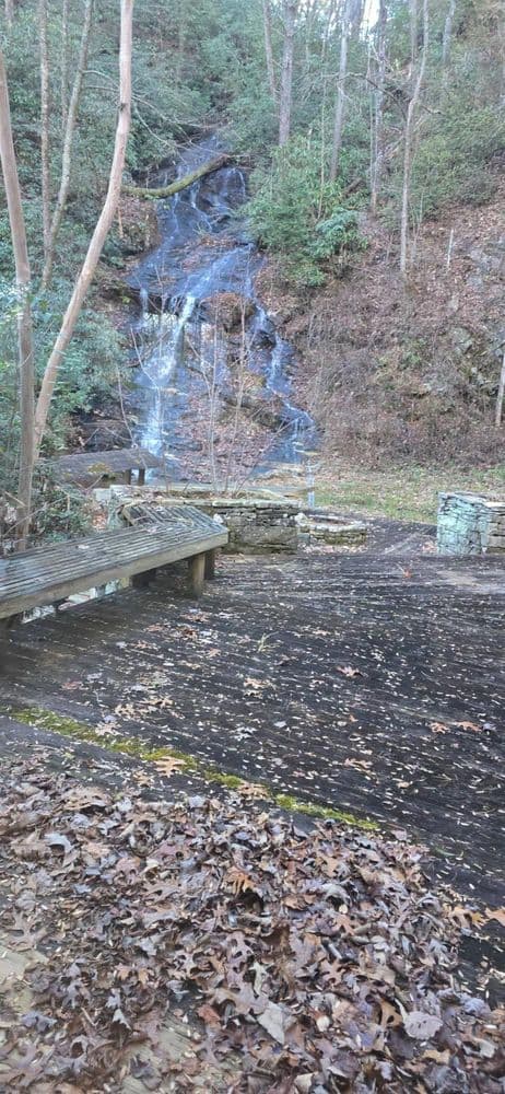 Scenic waterfall with wooden platform surrounded by autumn leaves and lush greenery.