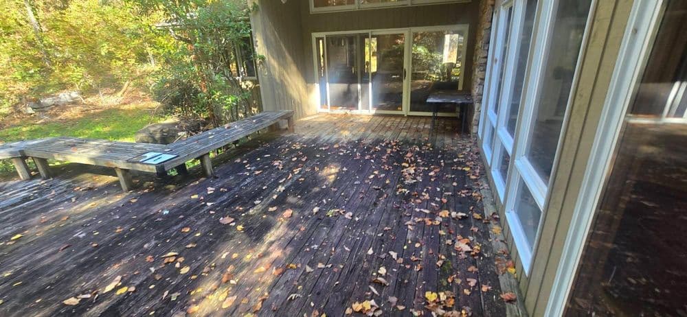 Deck area of a rustic cabin surrounded by fall foliage and scattered leaves.