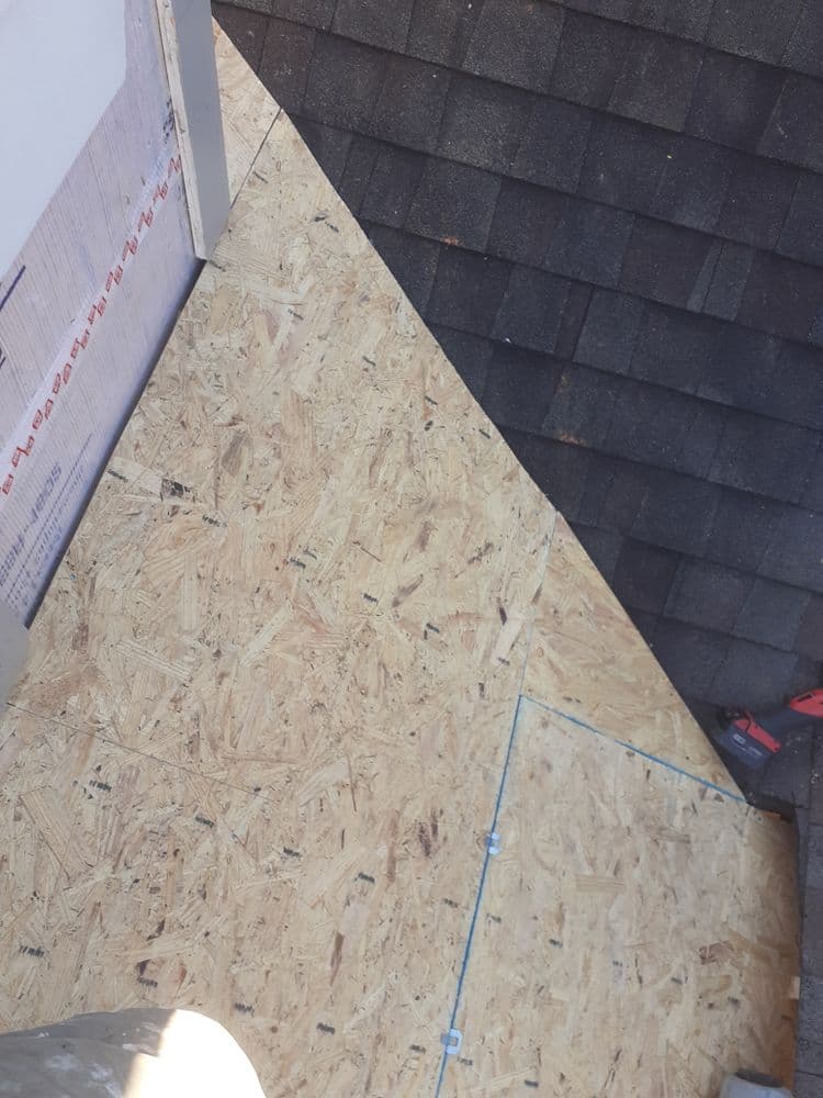 Newly installed OSB sheathing on a roof corner, showing shingles and construction tools.