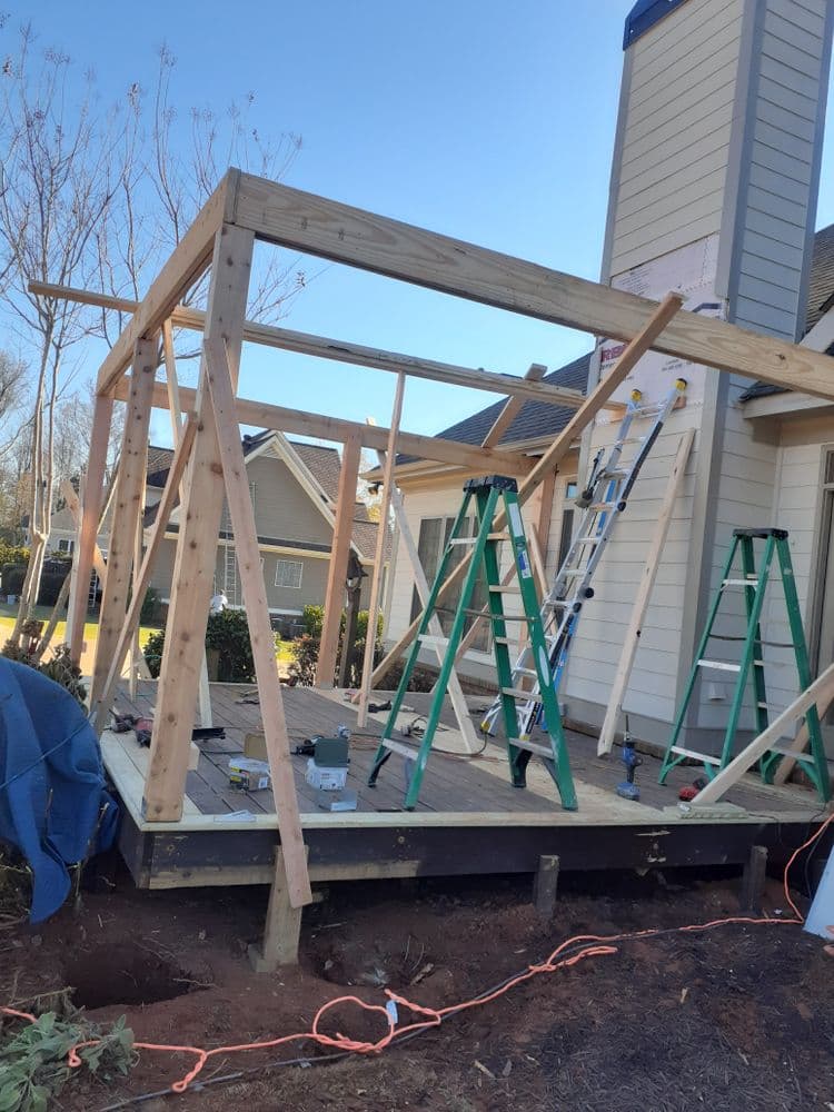 Wooden frame construction of a porch extension with ladders and tools on site.