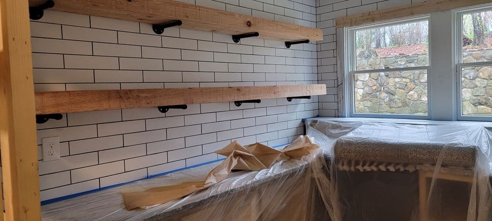 Modern kitchen renovation with wooden shelves, white subway tiles, and new countertop under plastic.