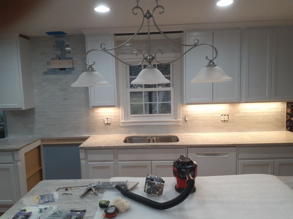 Modern kitchen renovation with white cabinets, pendant lights, and tools on countertop.