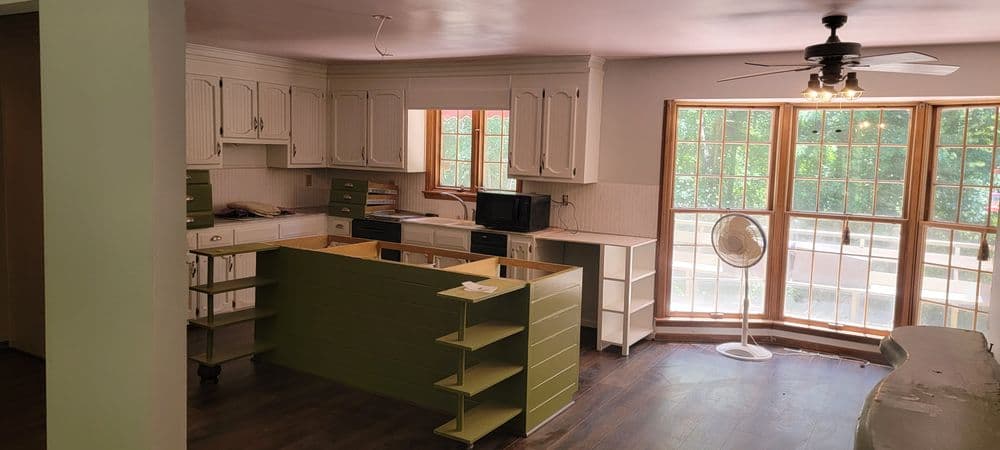Open kitchen space with white cabinets, green island, and large windows for natural light.