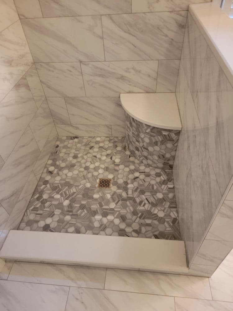 Modern shower design featuring marble walls and patterned tile floor with a built-in bench.