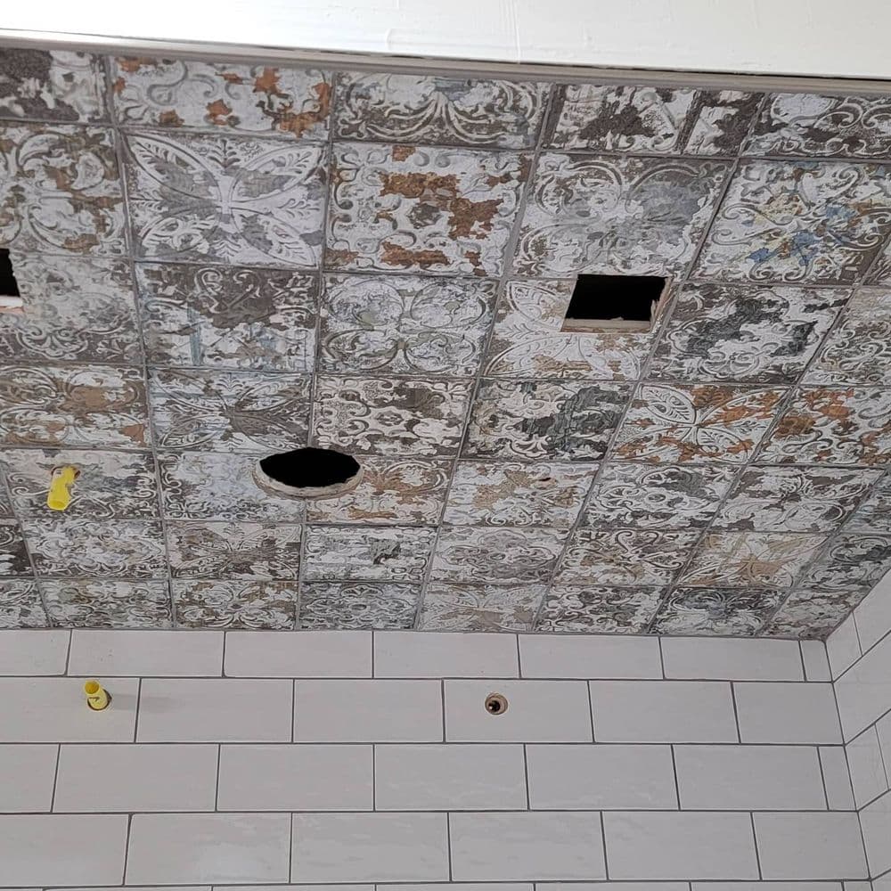 Vintage patterned ceiling tiles with two holes, above white tiled walls.