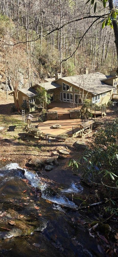 Secluded mountain cabin with deck by a stream, surrounded by forested woods.