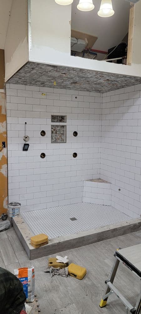 Modern shower renovation with white subway tiles, gray floor, and ceiling lights.