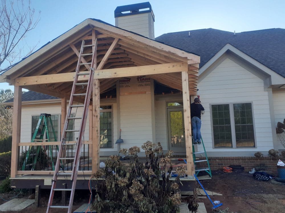 Construction of a wooden porch addition on a house with scaffolding and a ladder.