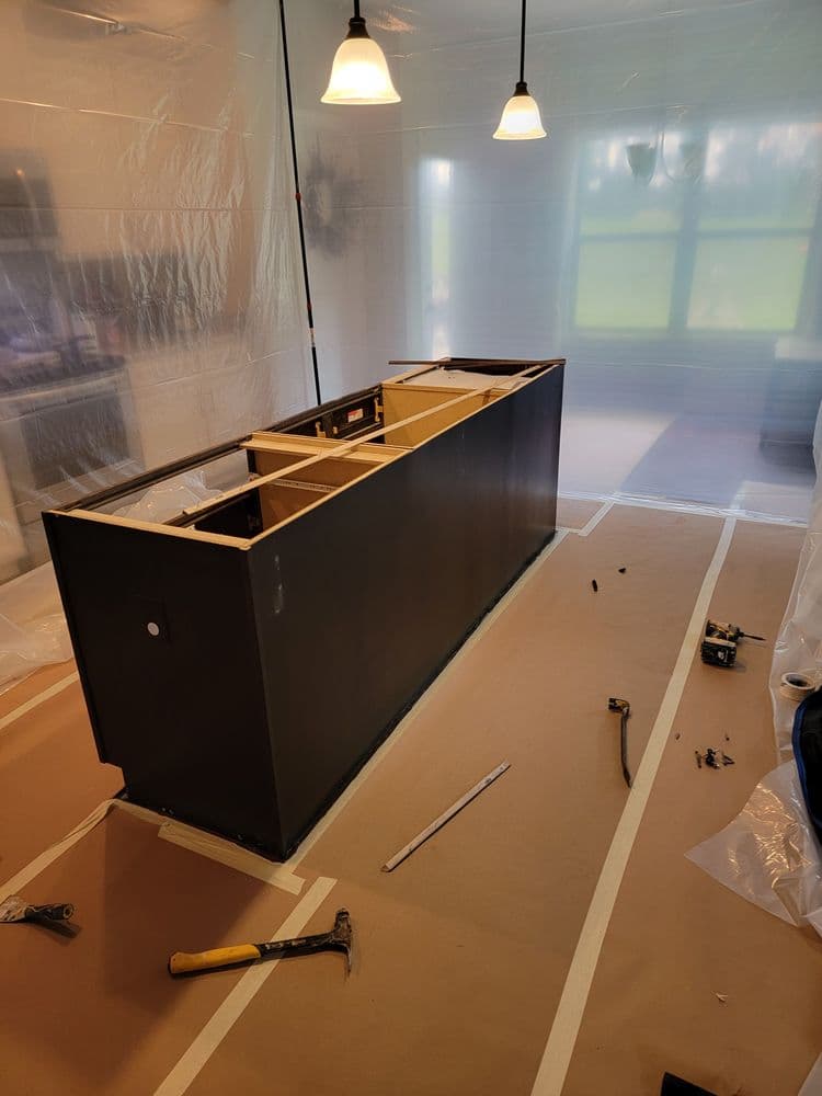 Home renovation: unassembled kitchen island surrounded by plastic sheeting and tools.
