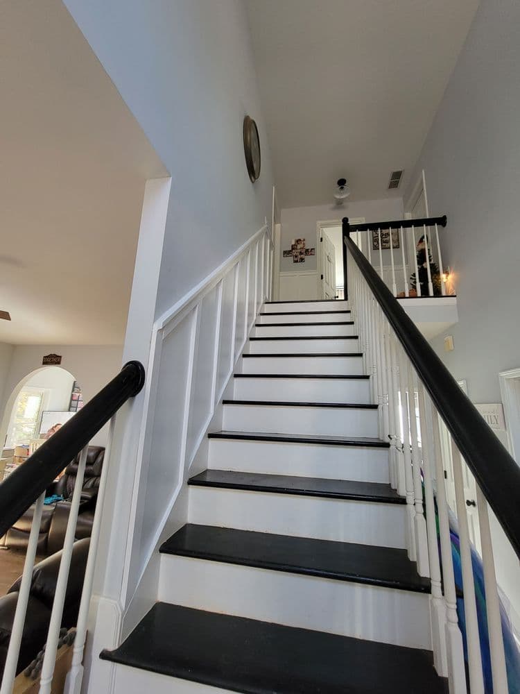 Modern staircase with black steps and white railing leading to an upper hallway. Bright interior.