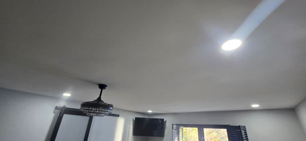 Modern room interior featuring ceiling lights, chandelier, and TV against a light backdrop.