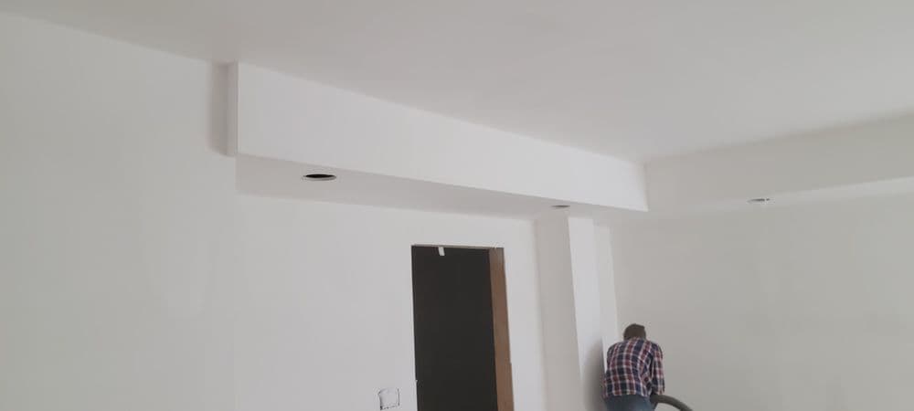 Man vacuuming in a newly painted room with white walls and ceiling details.