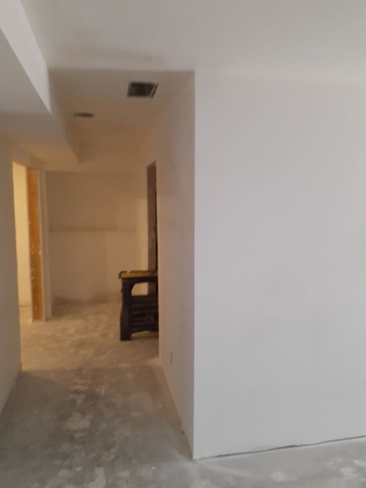 Empty, recently renovated hallway with white walls and unfinished flooring.