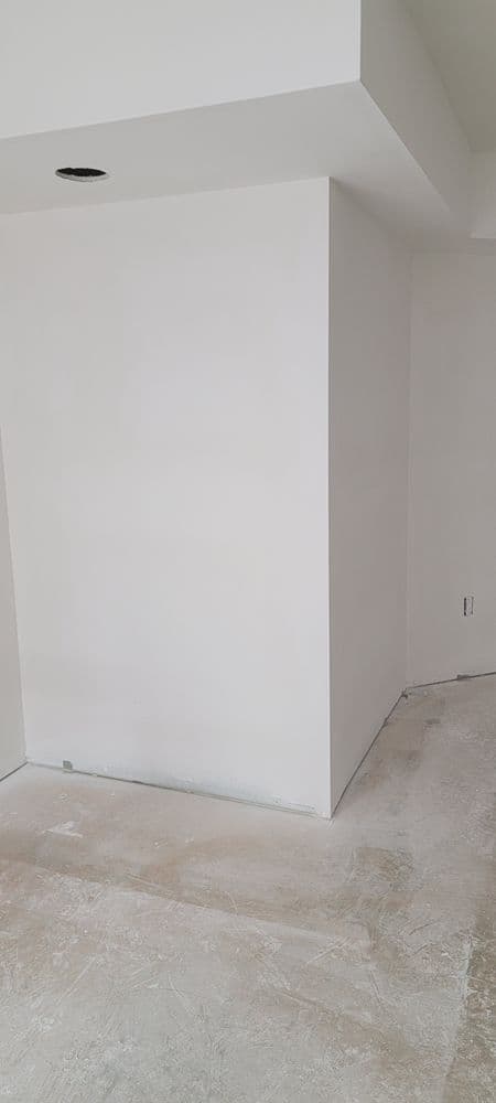 Empty room with white walls and unfinished flooring, featuring a corner view and ceiling lights.